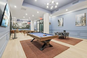 A pool table is in the middle of a room with a blue wall and a painting of a cityscape.